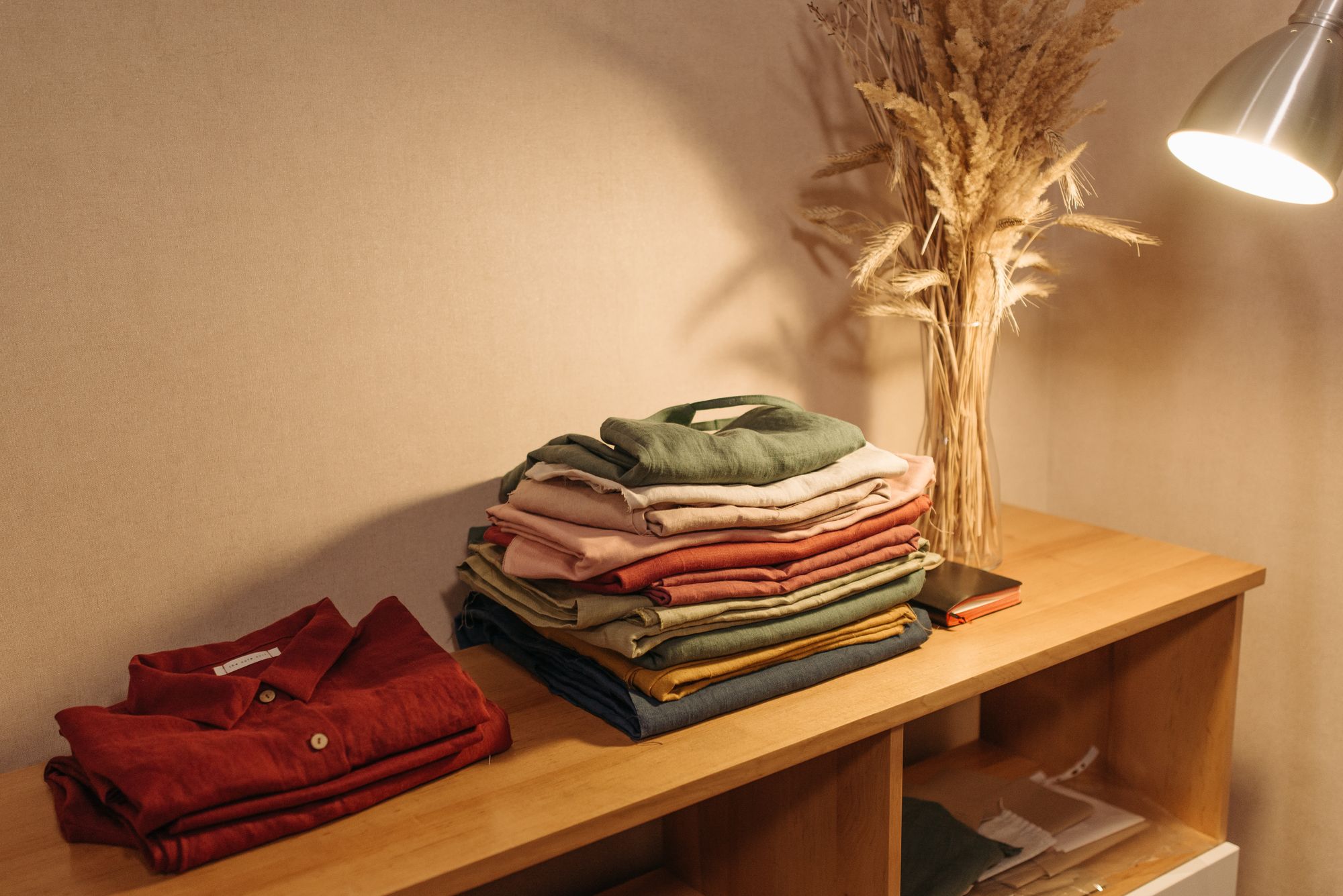 Peças de roupa dobradas sobre um aparador de madeira, sob luz quente de luminária.